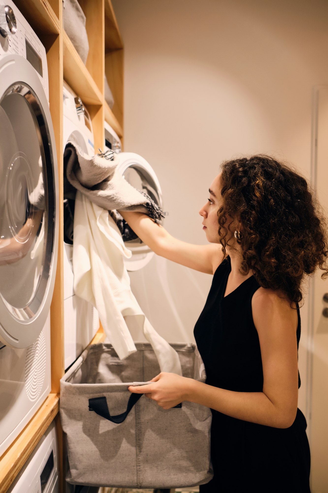Side view of attractive girl loading clothes into washing machine in modern self-service laundry